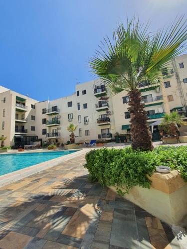 a palm tree in front of a building with a pool at Pretty 2 bedroom Apartment with shared Pool in St. Paul's Bay