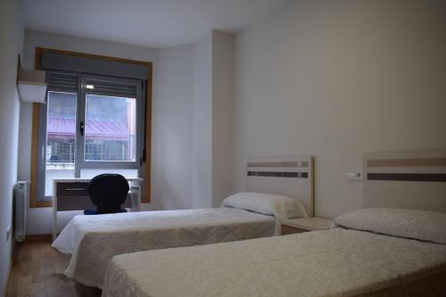 a room with two beds and a desk and a window at Apartamento centro Villagarcía. in Vilagarcia de Arousa