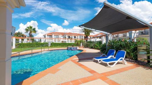 a swimming pool with two blue chairs next to a house at Breakers Block 5 Unit 6 in Yamba