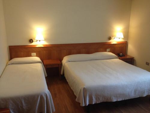 ファーノにあるHotel Cristalloのベッド2台、壁に照明2つが備わるホテルルームです。