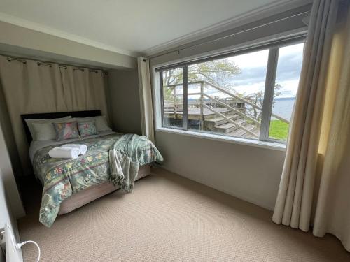 a bedroom with a bed and a large window at Lakeside & Tennis Court Paradise in Rotorua