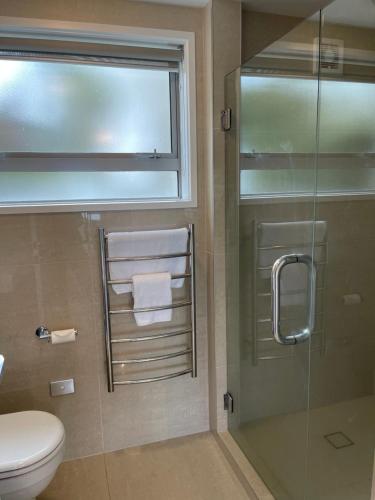baño con ducha, aseo y puerta de cristal en Lakeside & Tennis Court Paradise, en Rotorua