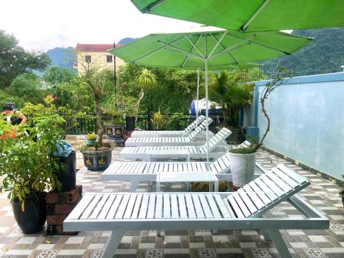 a row of white benches with a green umbrella at Phong Nha Green Homestay in Phong Nha