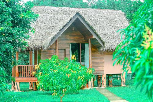 a wooden house with a grass roof and a bench at Sigiriya Water Cottage in Sigiriya