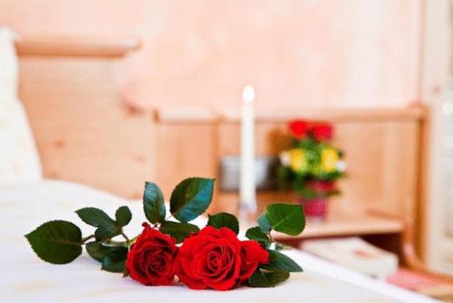 a candle and a bouquet of red roses on a bed at Pension Ederhof in Jochberg