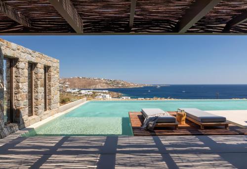 a swimming pool with two lounge chairs and the ocean at Untold Mykonos in Mikonos