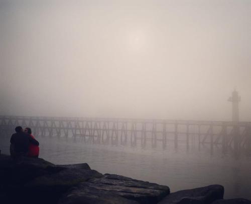 two people sitting on the edge of a pier in the fog at La Chambre du 21 in Trouville-sur-Mer