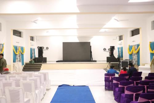 a room with white chairs and a stage with a screen at Vijayam Resort in Nāthdwāra