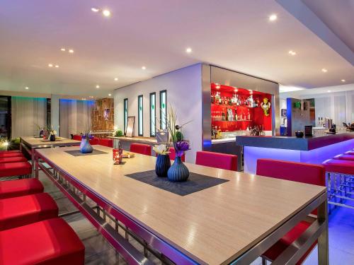un restaurante con una mesa larga y sillas rojas en ibis Styles Karlsruhe Ettlingen, en Ettlingen