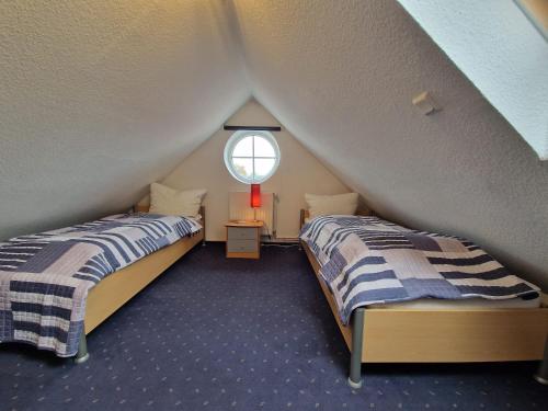 two beds in a attic room with a window at Ferienhaus Backbord im Bootshaus in Neßmersiel