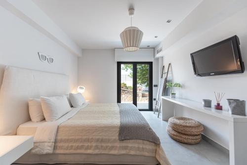 a white bedroom with a bed and a flat screen tv at Villa Soligia Blue in Pefkali