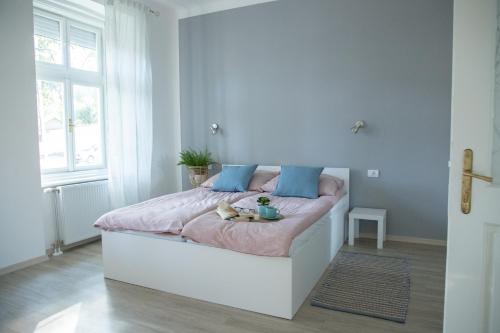 um quarto branco com uma cama com lençóis cor-de-rosa e almofadas azuis em Apartmani 64 em Sombor