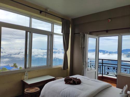 a bedroom with large windows and a bed with white sheets at Hotel High Ground Inn Sarangkot in Pokhara