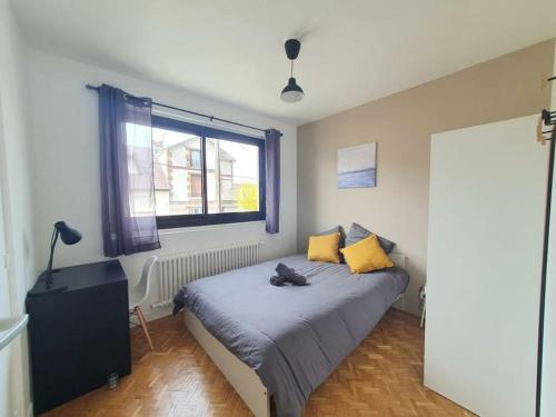 um quarto com uma cama com almofadas amarelas e uma janela em L'Orchidée - Cosy Flat, 20min From Paris em Drancy