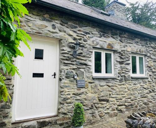 a stone house with a white door and two windows at Orchard Cottage in Corwen