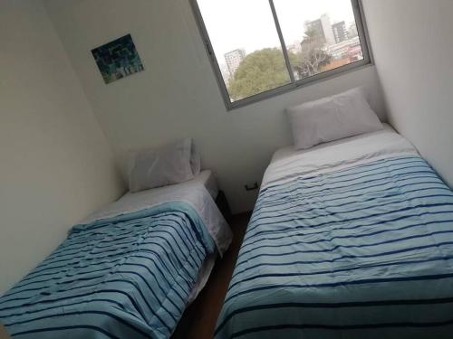 Duas camas num pequeno quarto com uma janela em Lindo y Espacioso Departamento muy cerca a Miraflores em Lima