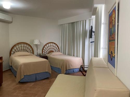 um quarto de hotel com duas camas e um sofá em Aparta Hotel Plaza del Sol em Santo Domingo