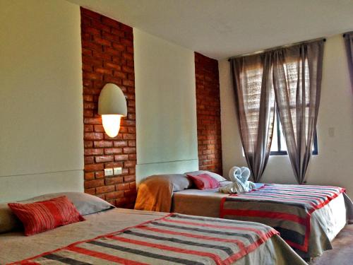 a bedroom with two beds and a brick wall at AXKAN PALENQUE, ALBERCAS, GASTRONOMIA MAR y TIERRA & TRAVEL AGENCY in Palenque