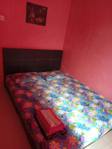 a bed with a colorful comforter and a red wall at HOMESTAY CAHAYA PUTERI in Tangga Batu
