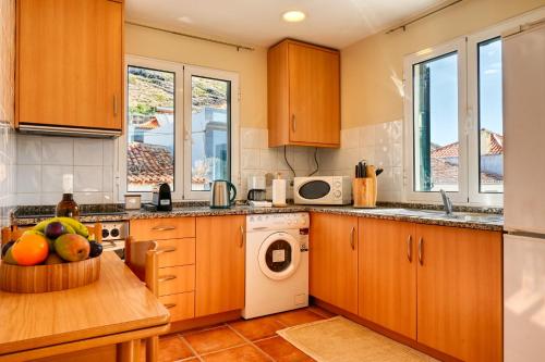 a kitchen with wooden cabinets and a table with a bowl of fruit at Largo dos Milagres, a Home in Madeira in Machico