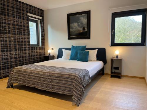 a bedroom with a bed with blue pillows and two windows at Chambres d’hôtes les Grisons in Houyet