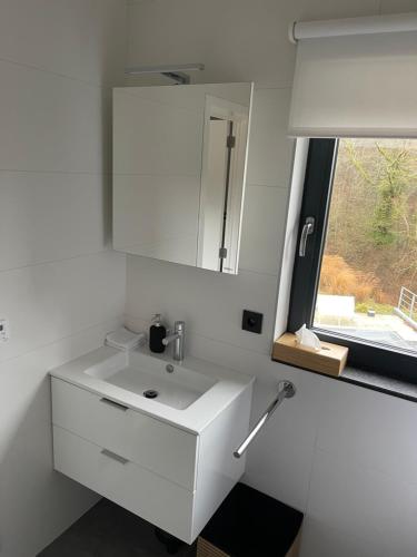 een witte badkamer met een wastafel en een raam bij Chambres d’hôtes les Grisons in Houyet