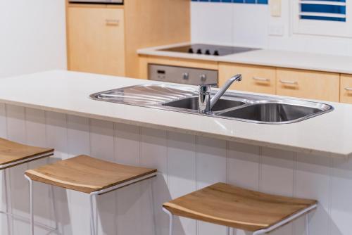 uma cozinha com um lavatório de aço inoxidável e bancos de madeira em Tropical Retreat in 2 Bedroom Townhouse em Noosaville