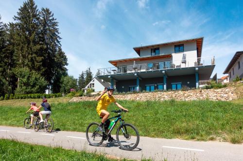 three people riding bikes down a road in front of a house at Rezidence Sunny Hill in Frymburk