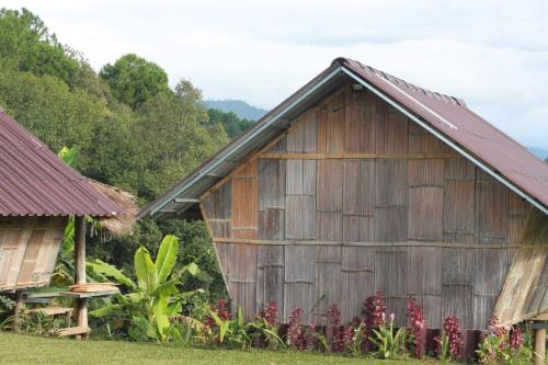 an old wooden barn with a bench and flowers at ไร่นิธิสุนทร nithisoonthon farmstay in Mae Hong Son