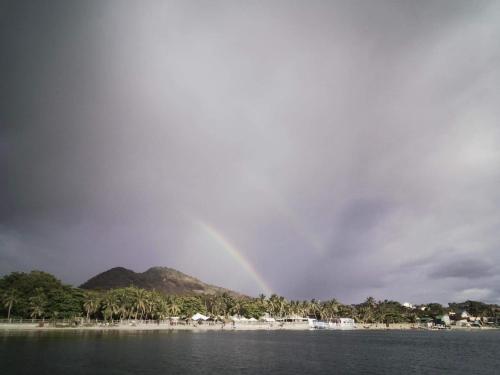 a rainbow in the sky over a beach at Manzil Anilao B&B in Mabini