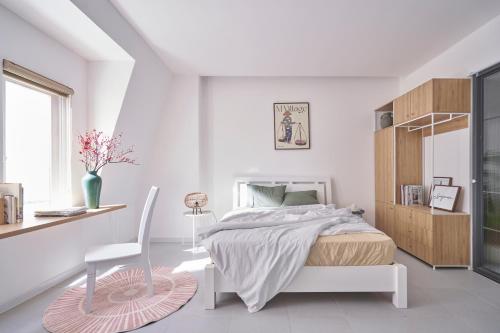 a white bedroom with a bed and a chair at M Village Nguyễn Văn Hưởng in Ho Chi Minh City