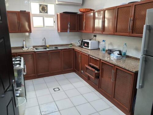 a kitchen with wooden cabinets and a white tile floor at Spacious Farm Stay with 3 bedroom & relaxing view in Remah