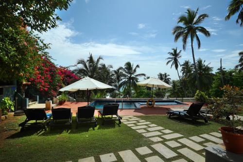 einen Garten mit Stühlen und Sonnenschirmen sowie einem Pool in der Unterkunft Getaway Beach Resort Kovalam in Kovalam