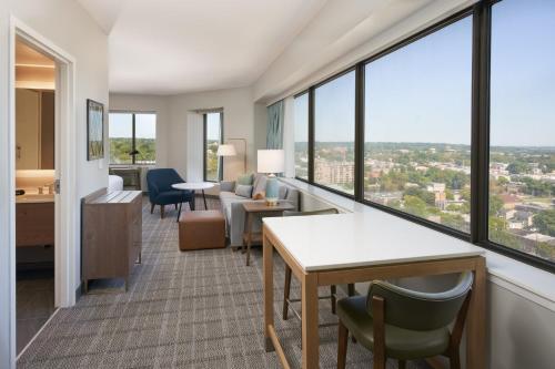 Habitación de hotel con escritorio, sillas y ventanas grandes. en Staybridge Suites Wilmington Downtown, an IHG Hotel, en Wilmington