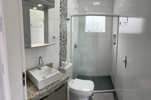 La salle de bains blanche est pourvue d'un lavabo et de toilettes. dans l'établissement Casa 3 quartos Bombinhas lado Mar ou AP de 2 quartos, à Bombinhas