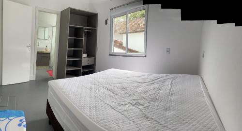 a white bedroom with a bed and a window at Casa 3 quartos Bombinhas lado Mar ou AP de 2 quartos in Bombinhas