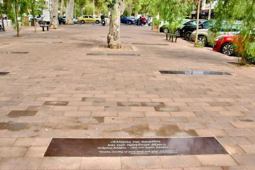 a plaque on a sidewalk with a tree and parked cars at Glyfada Path of Poets in Athens