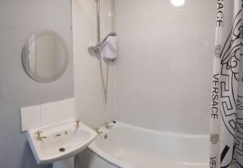 ein weißes Badezimmer mit einem Waschbecken, einer Badewanne und einem Spiegel in der Unterkunft Cheerful 3 Bedroom Apartment in Nottingham