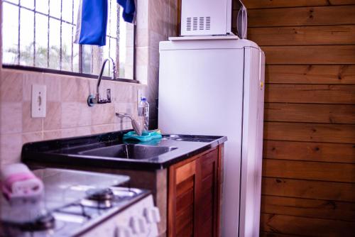 a kitchen with a sink and a white refrigerator at Pousada Chalés Beach - Praia do Rosa in Praia do Rosa