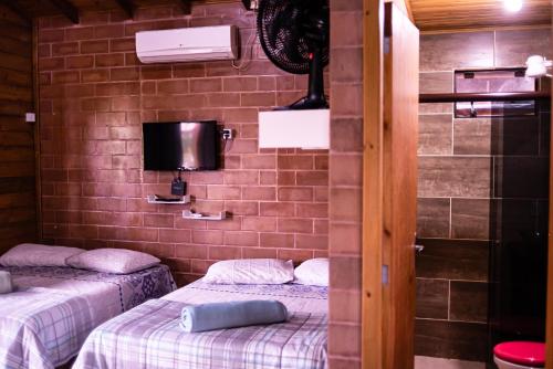 a room with two beds and a tv on a brick wall at Pousada Chalés Beach - Praia do Rosa in Praia do Rosa
