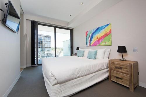 a white bedroom with a large bed and a tv at Aurora 14 in Canberra