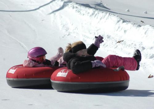 two children are riding on a tube in the snow at 2 Lake Cabins Poolhottub Game Room & Courts in Highland Lake