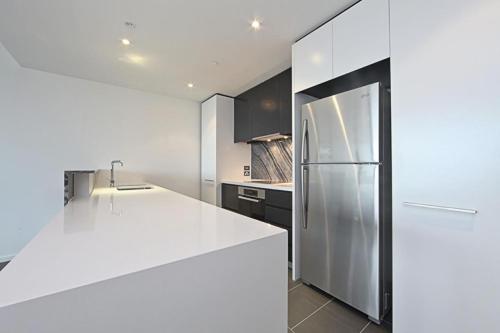La cuisine est équipée de comptoirs blancs et d'un réfrigérateur. dans l'établissement The ApARTments 403 Canberra City ACT, à Canberra
