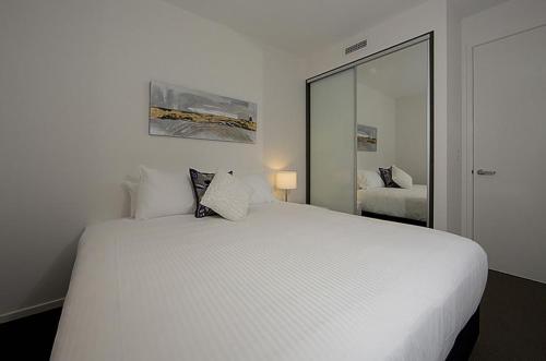 a bedroom with a large white bed with a mirror at Manhattan 303 Canberra City ACT in Canberra