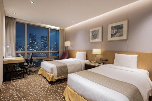 a hotel room with two beds and a desk and a window at Holiday Inn Incheon Songdo by IHG in Incheon