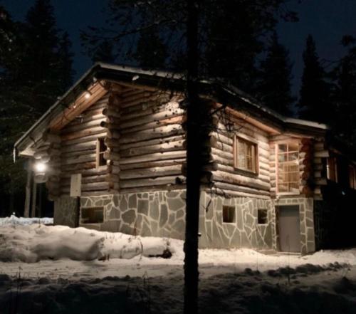 une cabane en rondins dans la neige la nuit dans l'établissement Kelogornitsa, à Kittilä