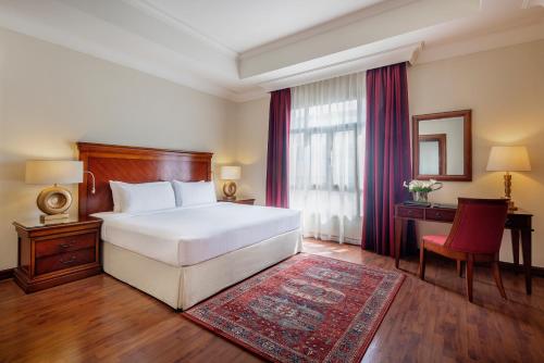 a bedroom with a bed and a desk and a window at Concorde Hotel Doha in Doha