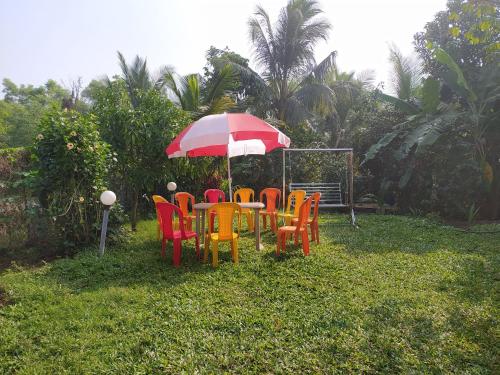 a table with colorful chairs and an umbrella at Kulswami Cottage Alibaug in Alibaug