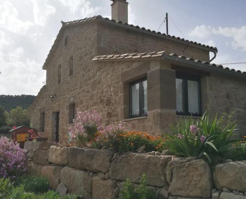 a stone house with a stone wall and flowers at Cal Sastre in Olíus