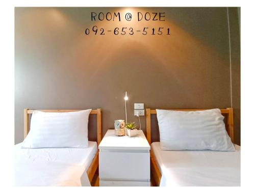 two beds with white sheets and a sign on the wall at Room@Doze in Nonthaburi